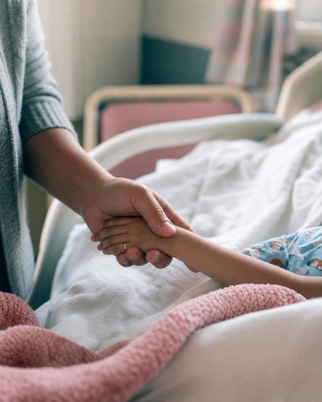 A parent gently holding their child's hand in a hospital room, captured in soft natural light
